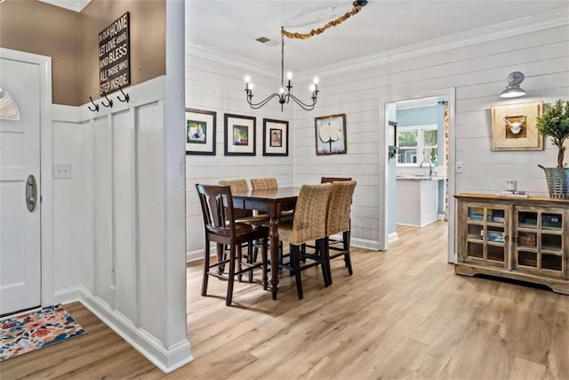 dining area featuring crown molding, sink, light hardwood / wood-style flooring, and a notable chandelier