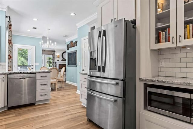 kitchen with crown molding, appliances with stainless steel finishes, white cabinetry, light stone countertops, and decorative backsplash