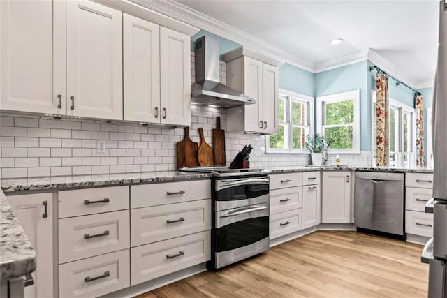 kitchen featuring light stone countertops, white cabinets, backsplash, stainless steel appliances, and wall chimney exhaust hood