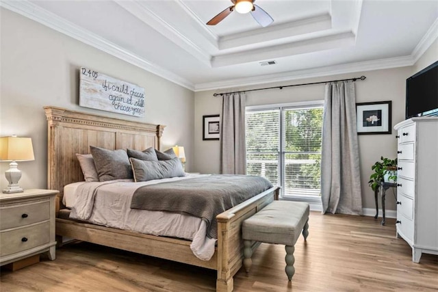 bedroom with wood-type flooring, ornamental molding, ceiling fan, and a raised ceiling