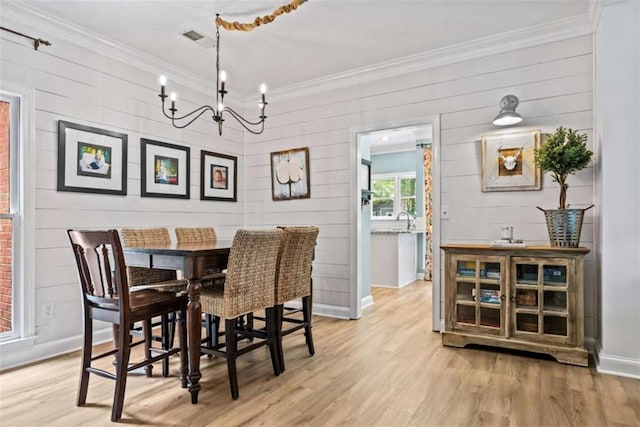 dining space featuring wood walls, light hardwood / wood-style flooring, ornamental molding, and a chandelier