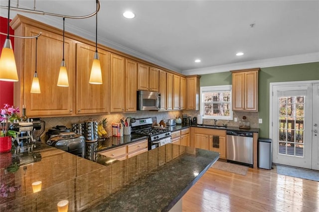 kitchen with decorative light fixtures, crown molding, appliances with stainless steel finishes, light wood-style floors, and a peninsula