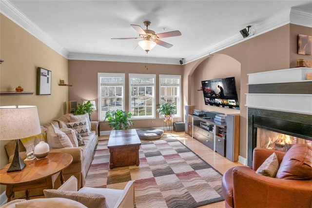 living area with ceiling fan, a lit fireplace, ornamental molding, and light wood-style flooring