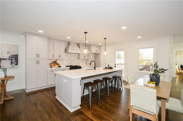 kitchen featuring pendant lighting, white cabinetry, custom range hood, and a center island with sink