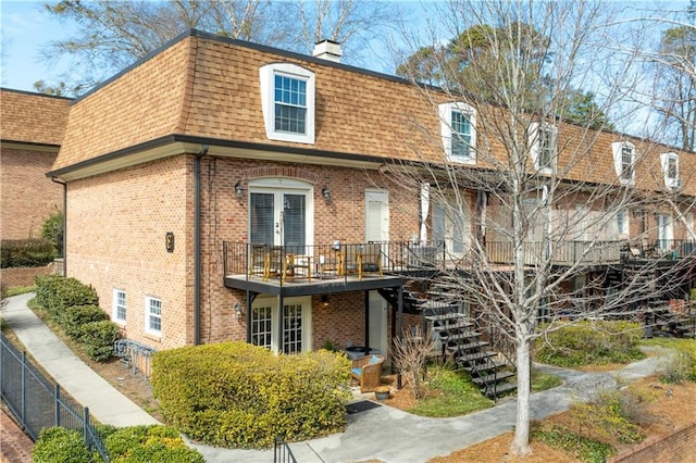 view of front of home with stairway, roof with shingles, mansard roof, a chimney, and french doors