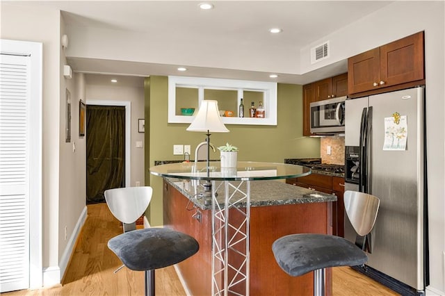 kitchen with visible vents, light wood-type flooring, a kitchen bar, stainless steel appliances, and a kitchen island with sink