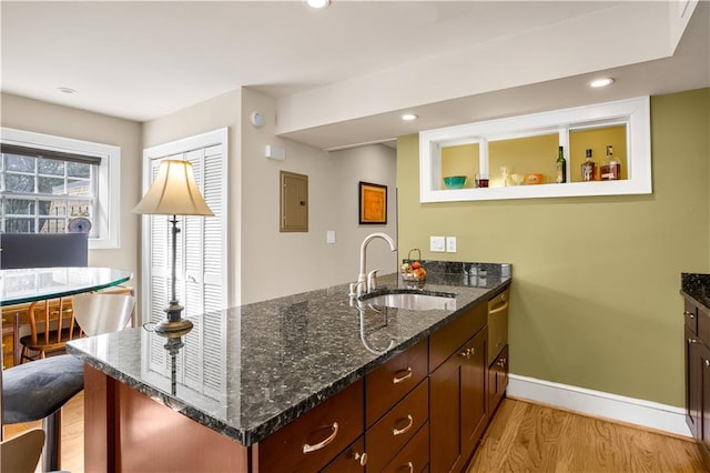 kitchen featuring light wood-style flooring, a sink, dark stone countertops, a peninsula, and baseboards