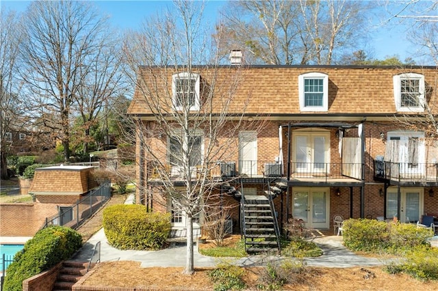 view of front facade with stairway, roof with shingles, french doors, a chimney, and mansard roof