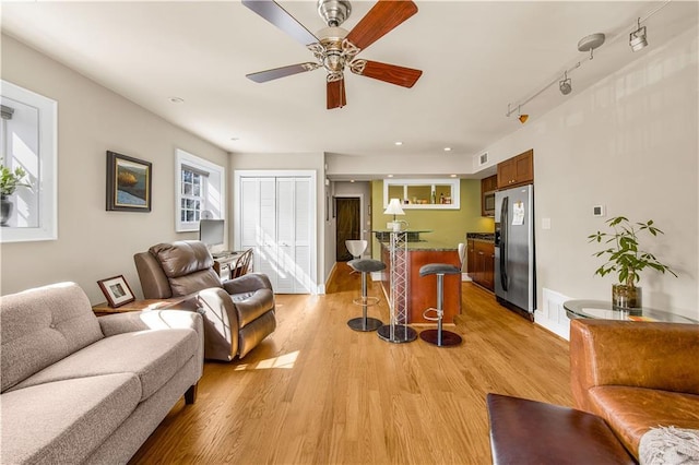 living area with a ceiling fan, rail lighting, light wood-style floors, and visible vents