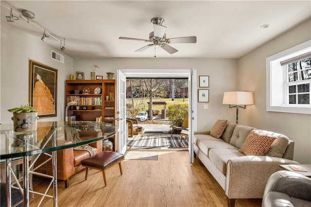 living room with ceiling fan, wood finished floors, visible vents, and a healthy amount of sunlight