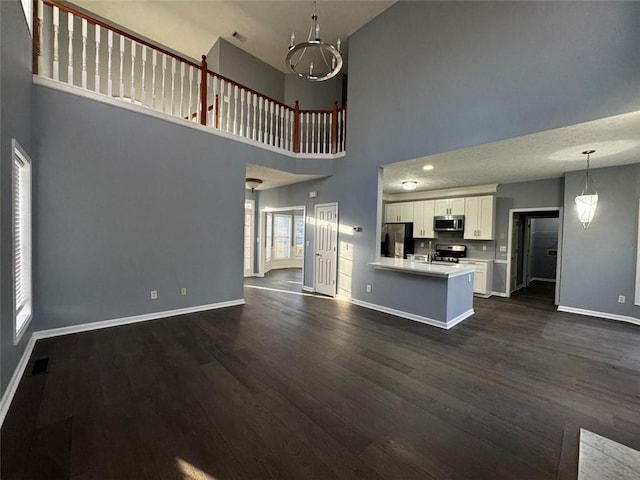 unfurnished living room featuring a high ceiling, dark hardwood / wood-style flooring, an inviting chandelier, and a healthy amount of sunlight