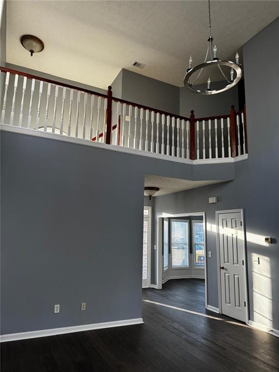 entryway featuring a towering ceiling, dark wood-type flooring, a textured ceiling, and an inviting chandelier