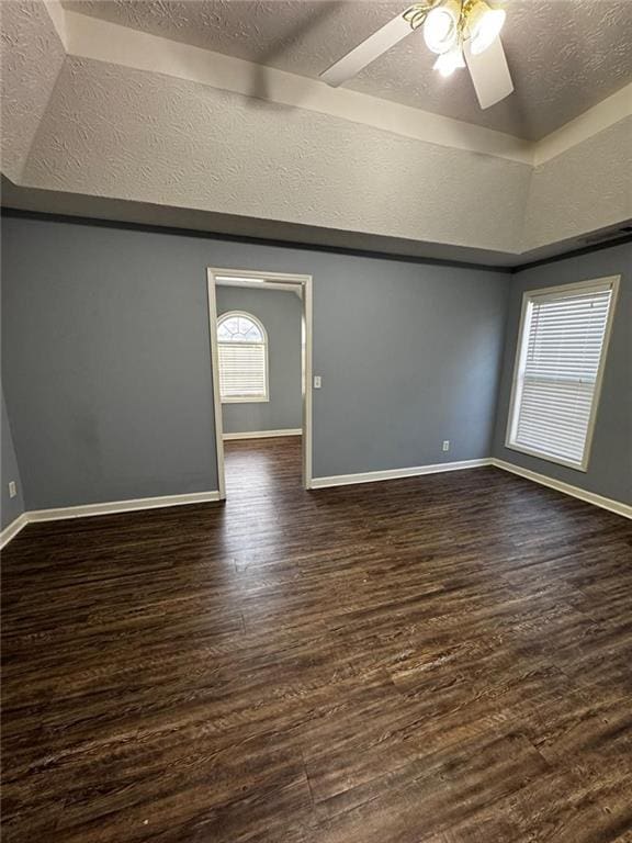 interior space with a textured ceiling, ceiling fan, a raised ceiling, and dark wood-type flooring