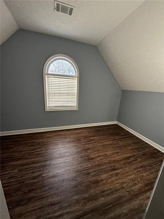 additional living space featuring a textured ceiling, dark hardwood / wood-style flooring, and vaulted ceiling