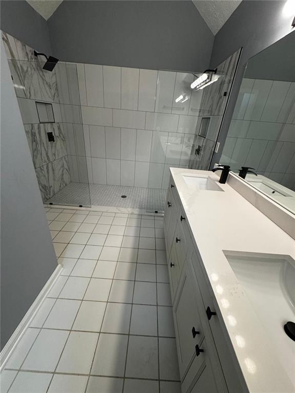 bathroom with a tile shower, tile patterned flooring, a textured ceiling, vaulted ceiling, and vanity