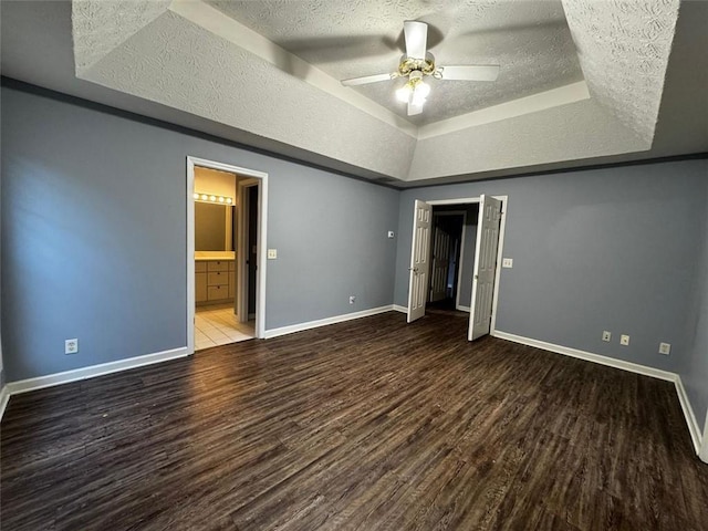 unfurnished bedroom featuring ensuite bath, ceiling fan, a raised ceiling, wood-type flooring, and a textured ceiling