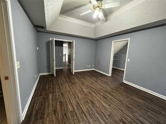 unfurnished bedroom with a textured ceiling, dark hardwood / wood-style flooring, a tray ceiling, and ceiling fan