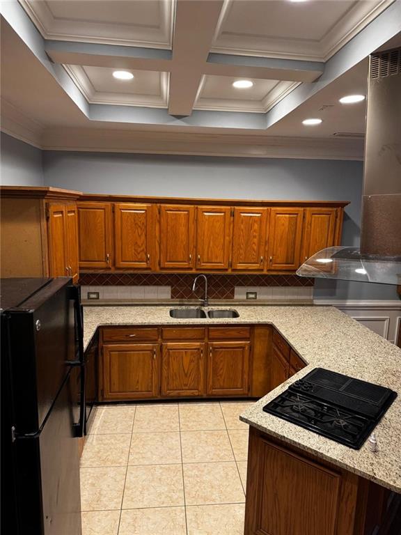 kitchen featuring light stone countertops, backsplash, coffered ceiling, black appliances, and sink