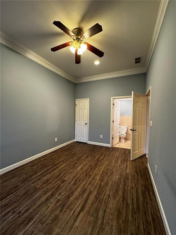 unfurnished bedroom featuring ensuite bath, ceiling fan, dark hardwood / wood-style flooring, and ornamental molding