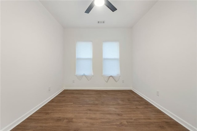 spare room featuring baseboards, visible vents, ceiling fan, and dark wood-style flooring