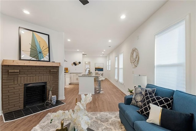 living area featuring a brick fireplace, light wood-style flooring, baseboards, and recessed lighting