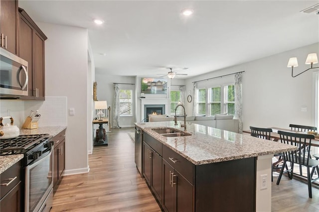 kitchen featuring ceiling fan, a sink, stainless steel appliances, open floor plan, and light wood-type flooring