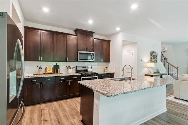 kitchen featuring appliances with stainless steel finishes, tasteful backsplash, a sink, and light wood-style floors