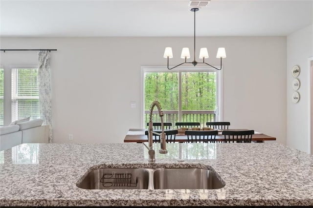kitchen featuring pendant lighting, light stone countertops, a sink, open floor plan, and an inviting chandelier