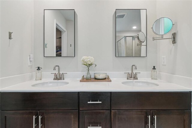 full bath featuring double vanity, a sink, a shower with shower door, and visible vents