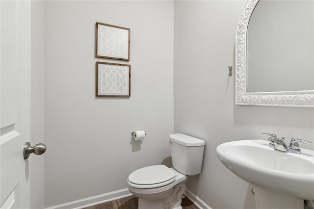 half bath with baseboards, a sink, wood finished floors, and toilet