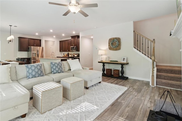 living room with ceiling fan, light wood-type flooring, stairway, baseboards, and recessed lighting