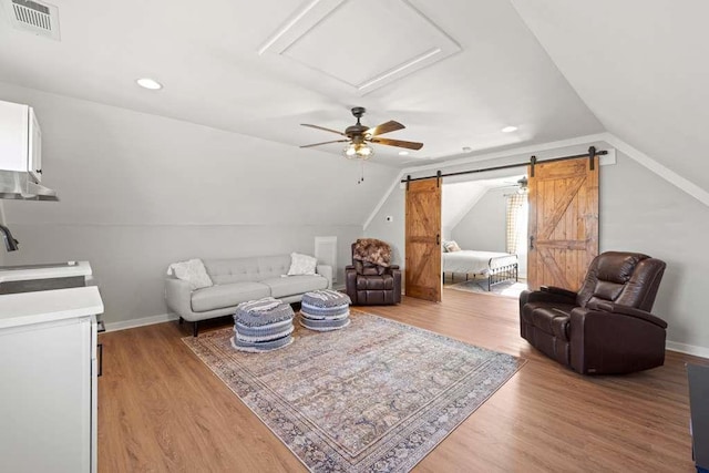 living room featuring sink, vaulted ceiling, a barn door, and light wood-type flooring