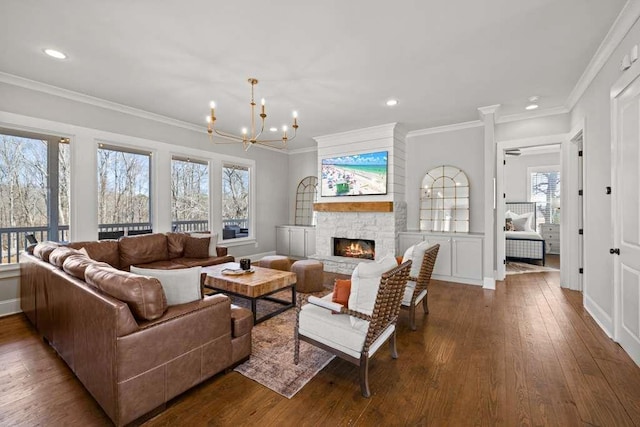 living room with dark wood-type flooring, ornamental molding, a fireplace, and an inviting chandelier