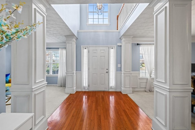 carpeted foyer entrance with crown molding, hardwood / wood-style flooring, decorative columns, and a decorative wall