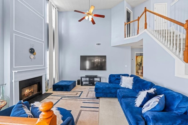 living room featuring carpet floors, a fireplace with flush hearth, visible vents, a ceiling fan, and stairway