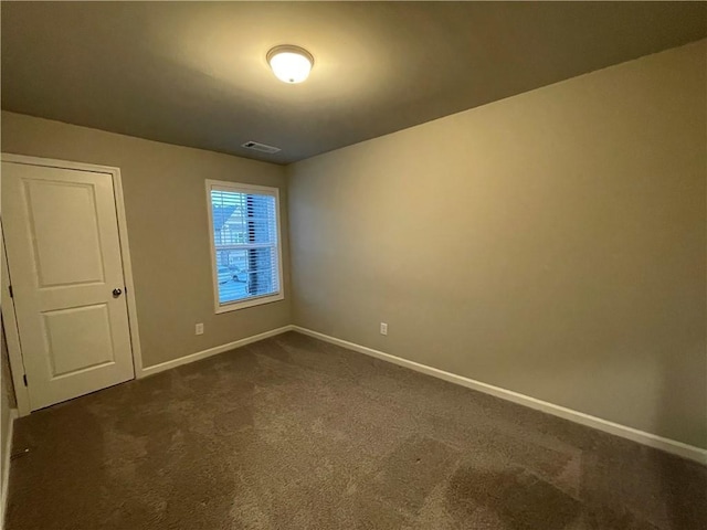 spare room featuring visible vents, dark carpet, and baseboards