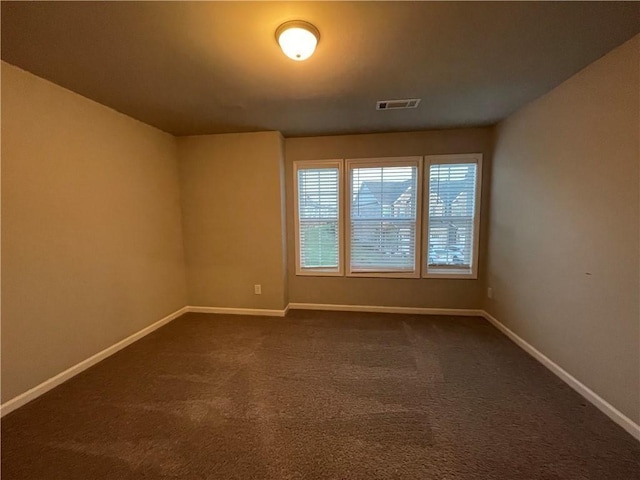 unfurnished room with visible vents, dark carpet, and baseboards
