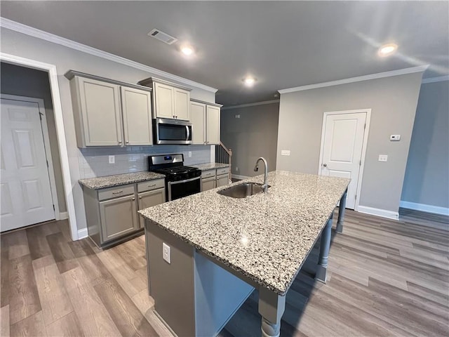 kitchen featuring appliances with stainless steel finishes, light wood-type flooring, a sink, visible vents, and a center island with sink