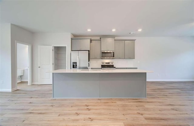 kitchen featuring gray cabinets, stainless steel appliances, light hardwood / wood-style floors, and a center island with sink