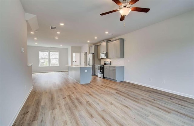 kitchen with appliances with stainless steel finishes, a kitchen island with sink, gray cabinetry, and light hardwood / wood-style flooring