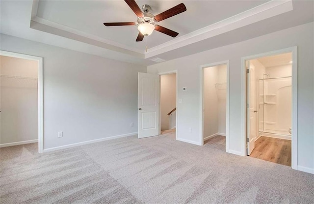 unfurnished bedroom featuring ensuite bathroom, a walk in closet, a raised ceiling, light carpet, and a closet