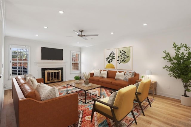 living room with ceiling fan, crown molding, a fireplace, and light wood-type flooring