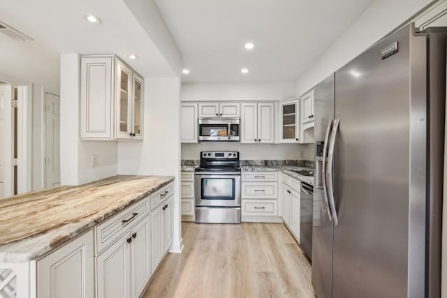 kitchen with white cabinetry, appliances with stainless steel finishes, light stone countertops, and light wood-type flooring