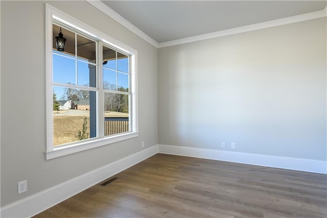 empty room featuring baseboards, visible vents, crown molding, and wood finished floors