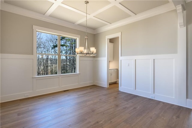 unfurnished dining area with a decorative wall, wood finished floors, and an inviting chandelier