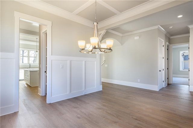 unfurnished dining area with a wainscoted wall, a decorative wall, crown molding, wood finished floors, and a notable chandelier