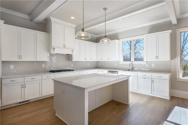 kitchen featuring black stovetop, beamed ceiling, light wood-style flooring, and a sink