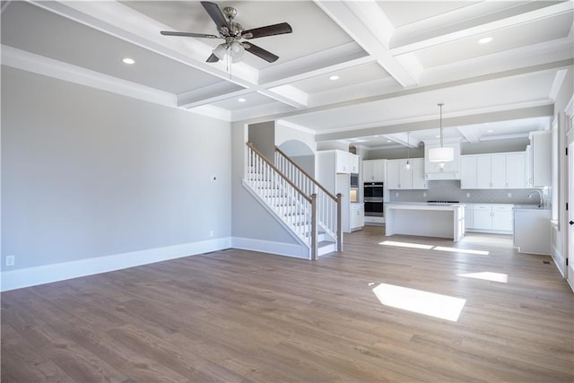 unfurnished living room featuring light wood-style flooring, stairway, and beamed ceiling