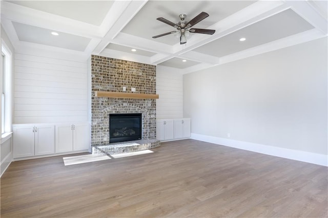 unfurnished living room featuring a brick fireplace, coffered ceiling, beam ceiling, a ceiling fan, and wood finished floors