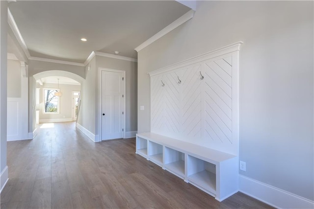 mudroom with arched walkways, crown molding, baseboards, and wood finished floors
